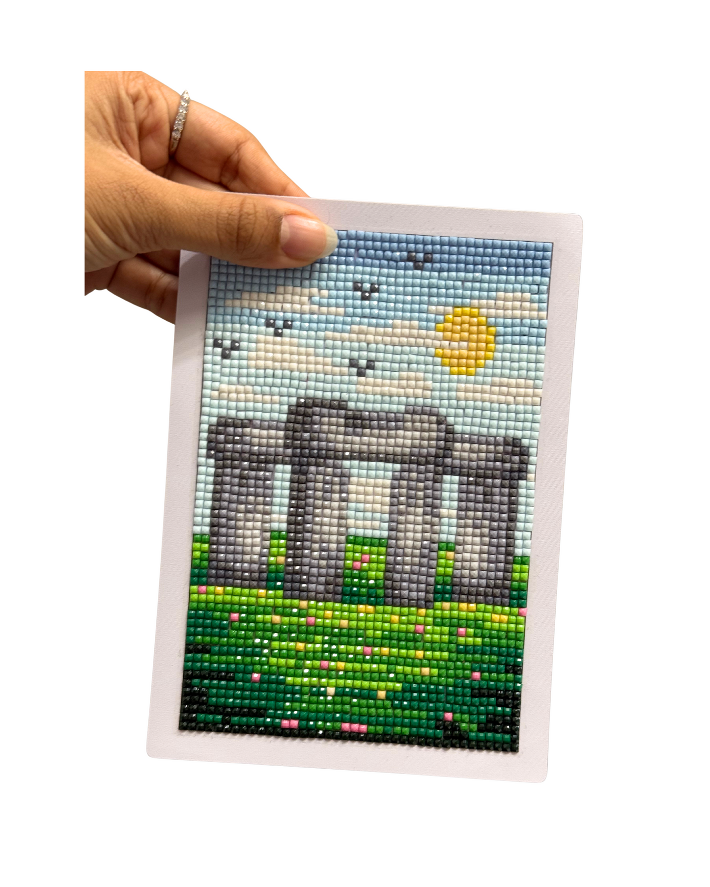 Hand holding a completed diamond painting of Stonehenge with a blue sky and sun.