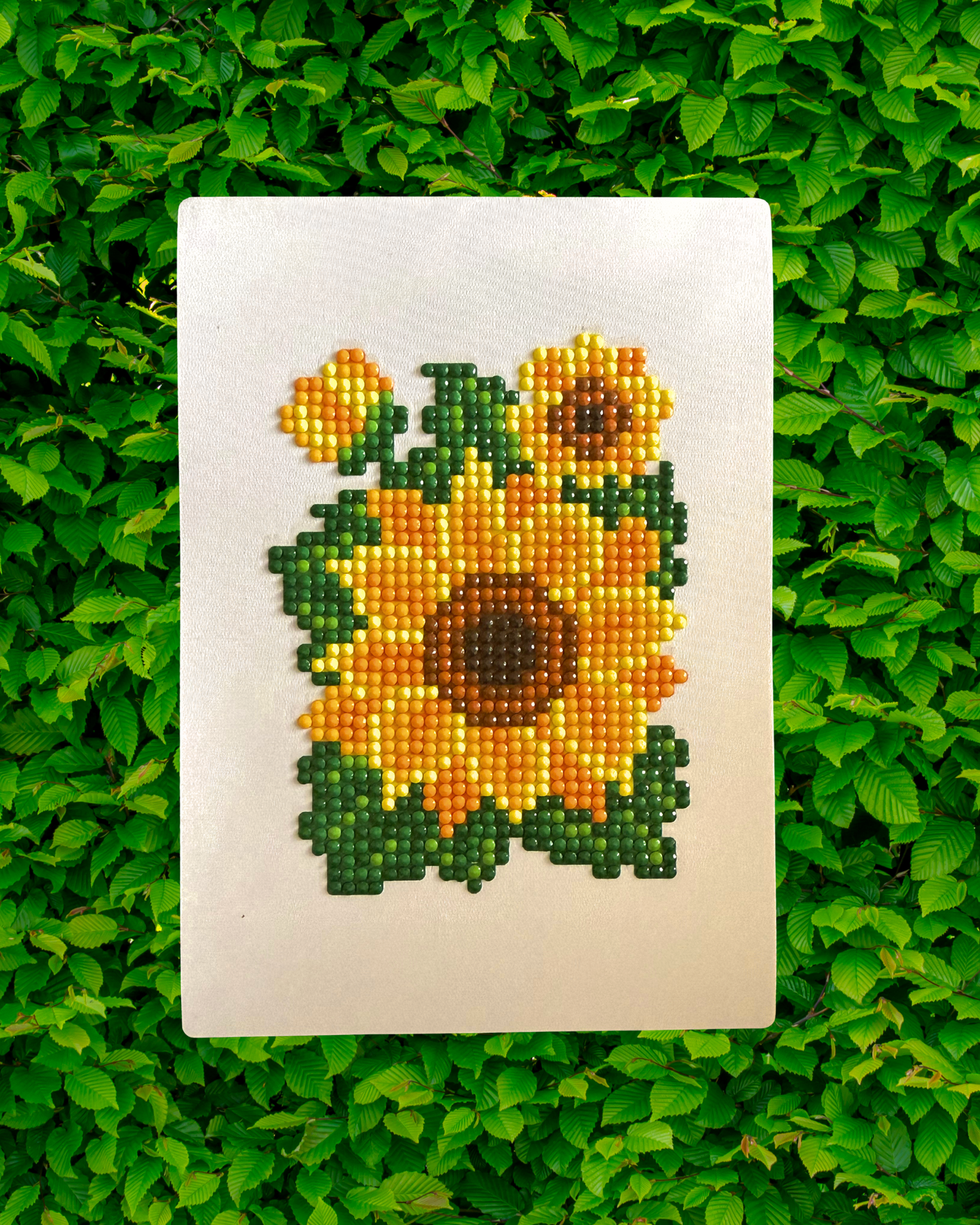 Completed diamond painting design on a white card with green leaves in the background